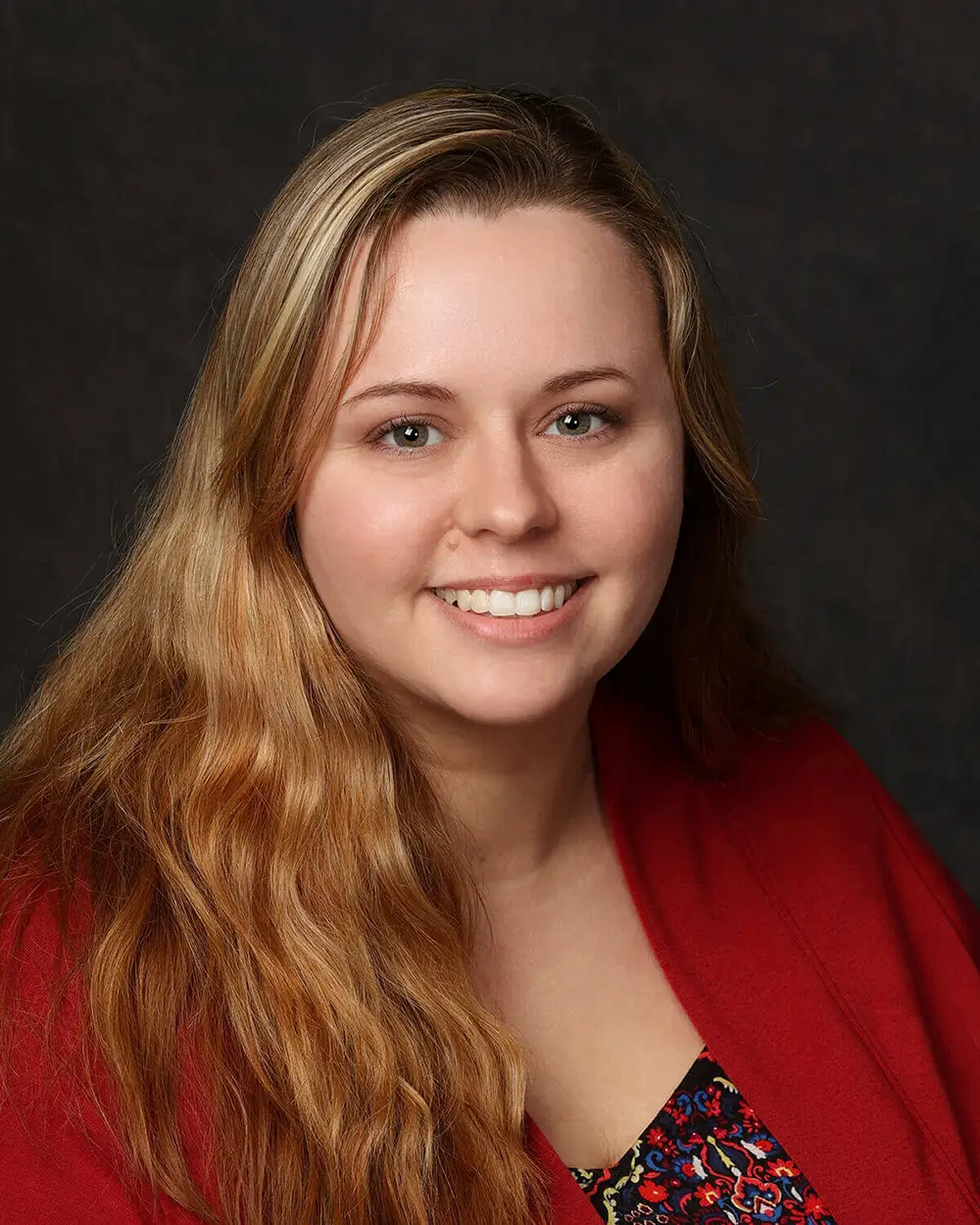 Woman with long blond hair smiles into camera in front of black background