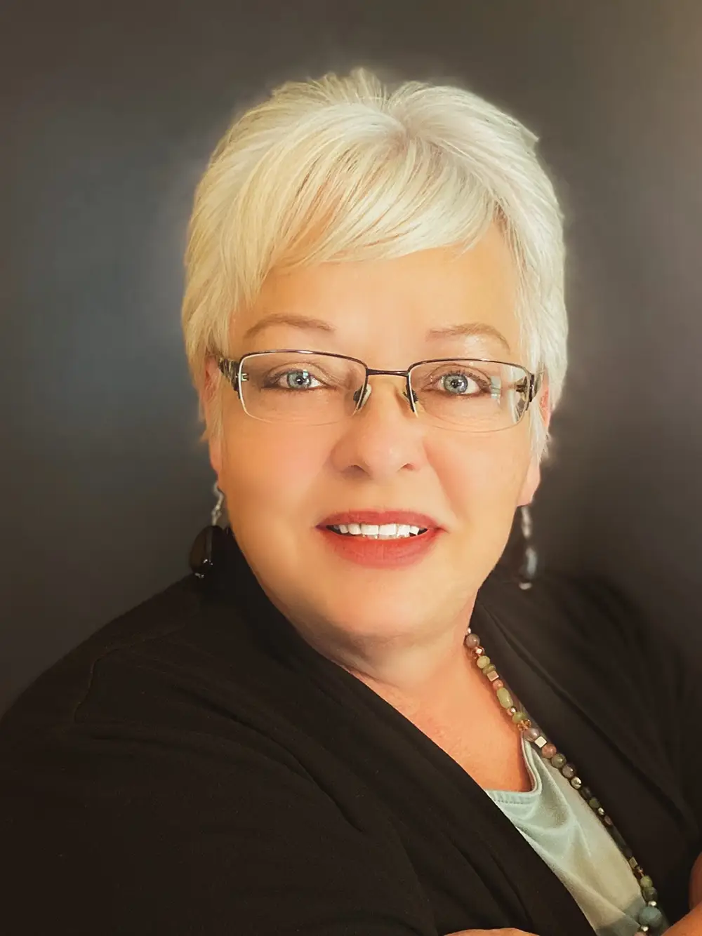 woman with short blond hair and glasses looks into camera and smiles slightly