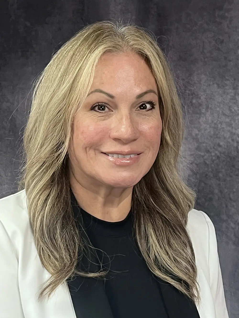Woman with long blond hair smiles into camera in front of grey background