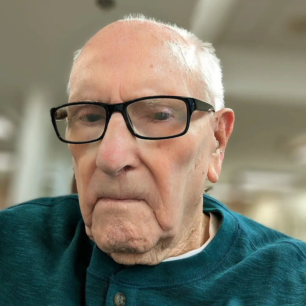 Elderly man wearing black rimmed glasses looks into the camera seriously