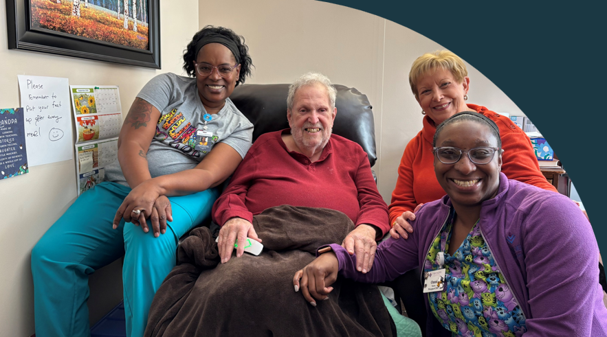 FPM resident sitting in recliner with his wife to his left and a health care worker on each side