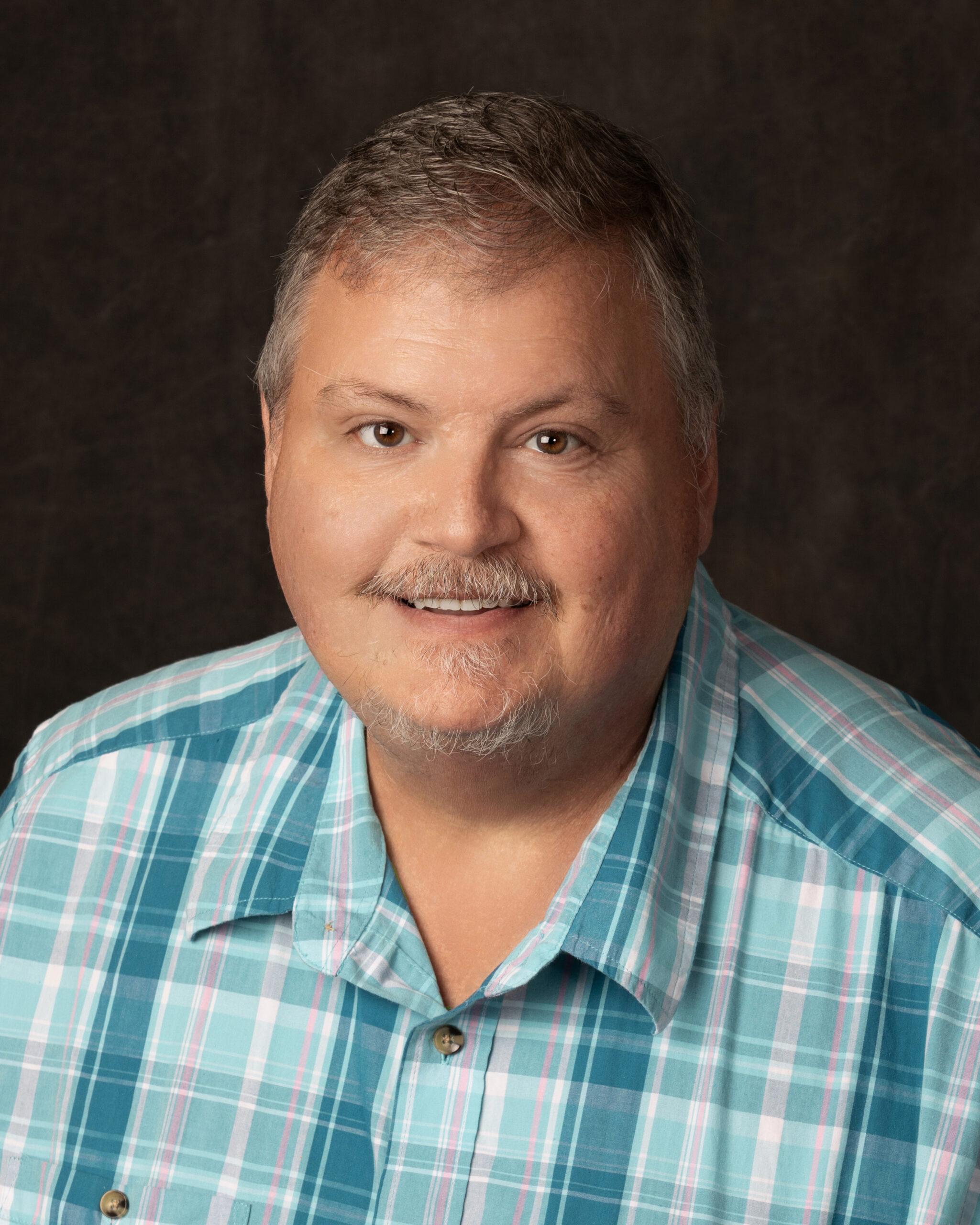 Stuart Griffiths – Sales, Social Services (Spring 2026) Man with mustache, wearing a teal checkered button down shirt smiles into camera