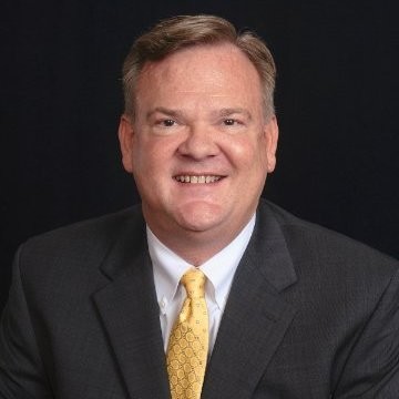 Man dressed in suit and yellow tie smiles into the camera in front of black background