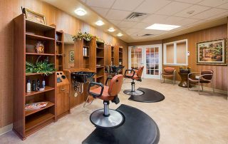A well-lit hair salon with two styling stations, brown chairs, wooden shelving with hair products, sinks, and framed artwork on the walls.